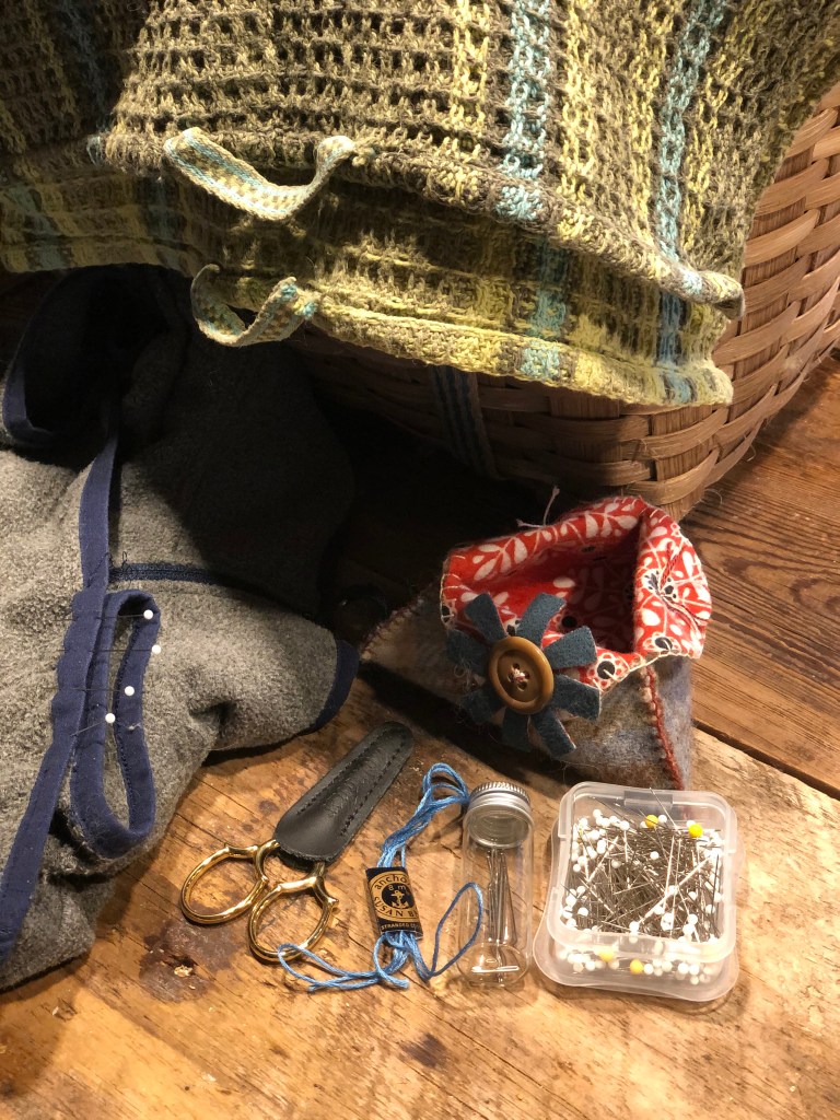 Picture of my mending in a basket, with scissors, bright blue embroidery thread, pins, needles and a triangular wool ‘thread catcher’ for my snippets